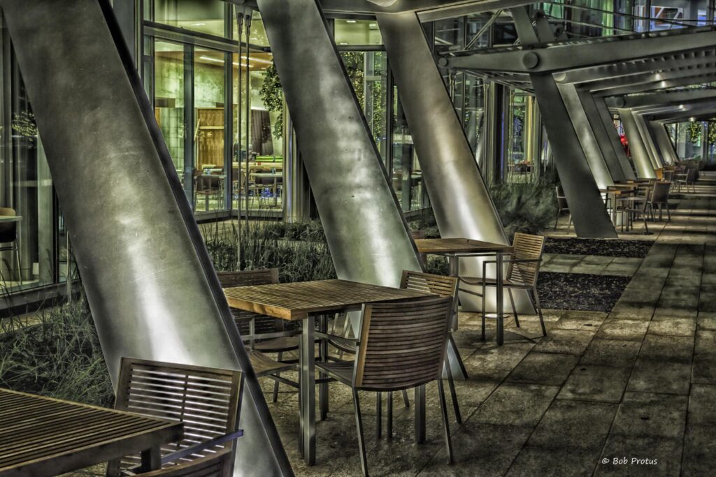 Interior of office building in Oklahoma City featuring several large steel beams and small wooden tables and chairs for meeting or eating. The space is otherwise empty.