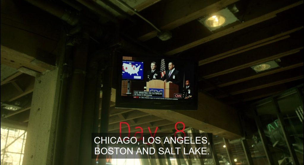 A frame from Contagion (2011) showing a TV monitor mounted to a wall and the on-screen text, Day 8, which is partially covered by the closed caption: Chicago, Los Angeles, Boston, and Salt Lake.
