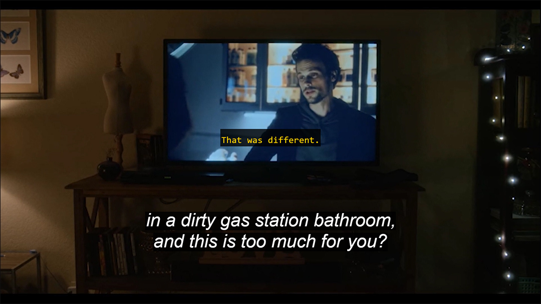 A frame from Horse Girl showing a TV screen, which includes a yellow caption, "That was different." At the bottom of the frame is a second caption track in white letters: "in a dirty gas station bathroom, and this is too much for you?"